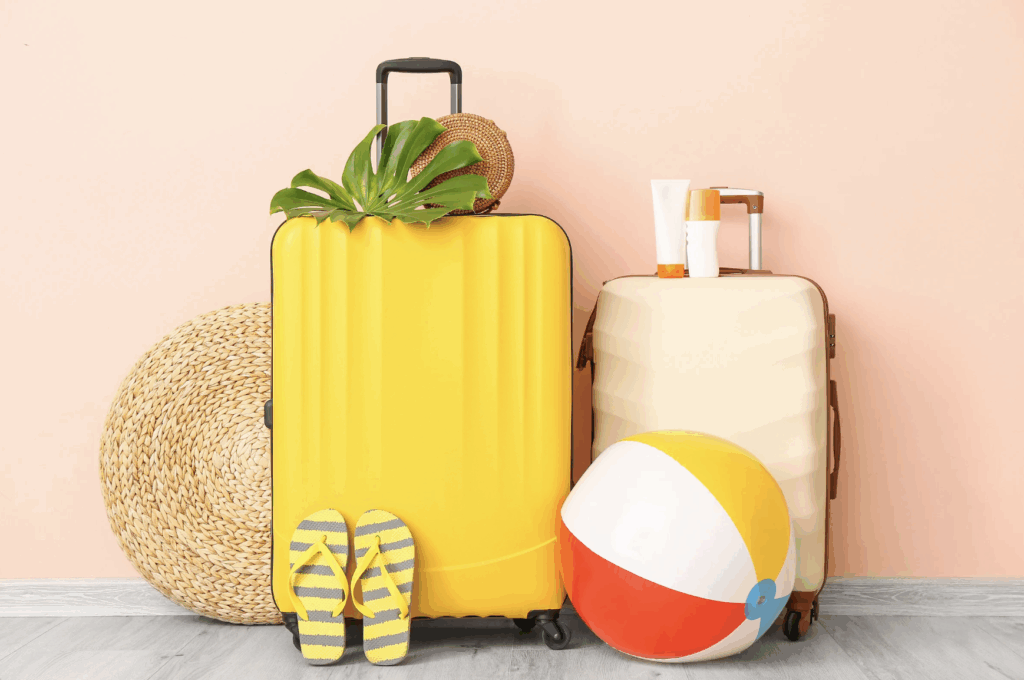 Bright yellow and cream suitcases with summer travel essentials including flip-flops, sunscreen, a beach ball, and a woven hat, perfect for a mindful, recovery-focused vacation.